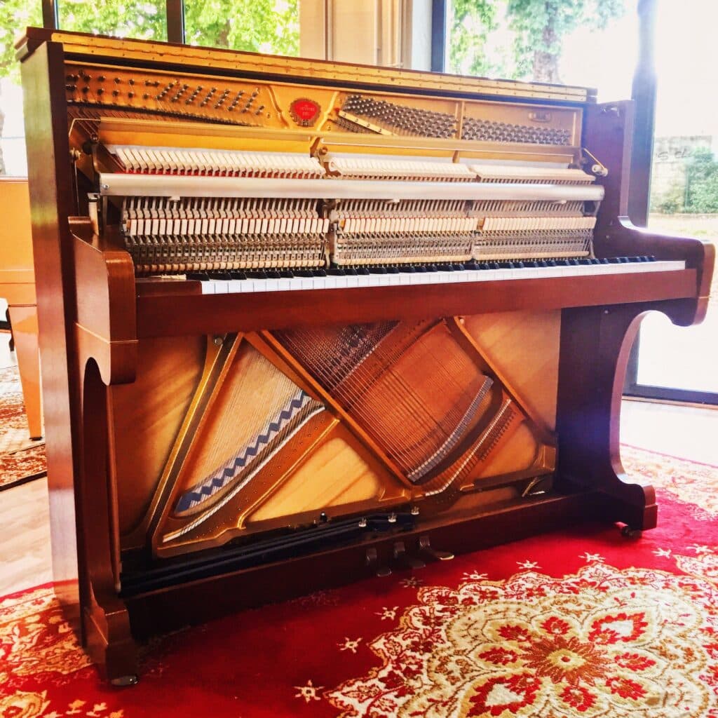 Piano droit acoustique ouvert montrant la mécanique et les cordes dans le showroom Bonnaventure à Caen