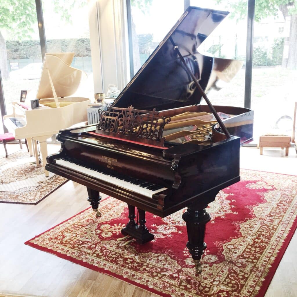Piano à queue ancien en bois foncé sur tapis rouge dans un atelier de pianos à Caen