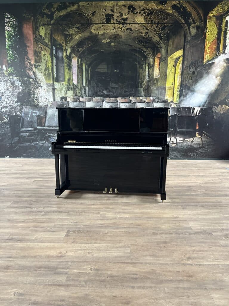 Piano droit Yamaha UX10A noir laqué en exposition devant un décor mural industriel